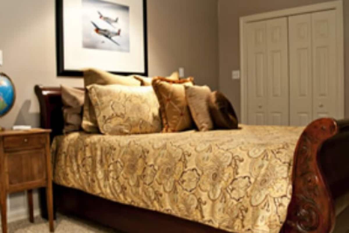 A bedroom with a large bed, a framed picture on the wall, a globe on a side table, and a wardrobe.