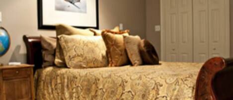 A bedroom with a large bed, a framed picture on the wall, a globe on a side table, and a wardrobe.