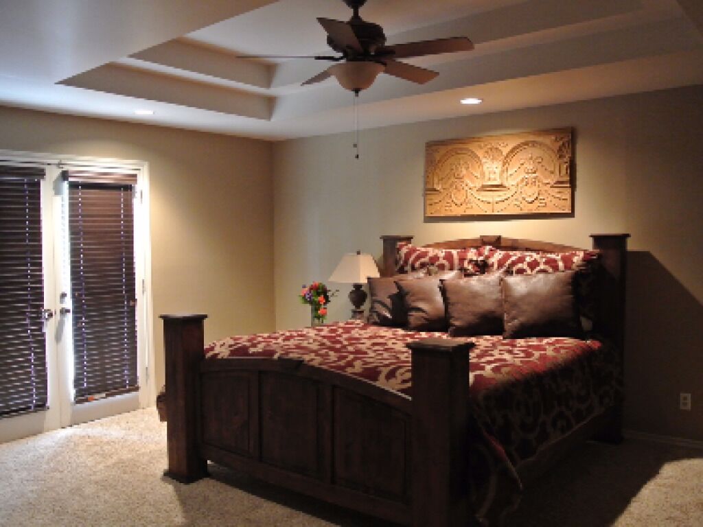 A bedroom with a wooden bed, a ceiling fan, and a wall-mounted artwork.