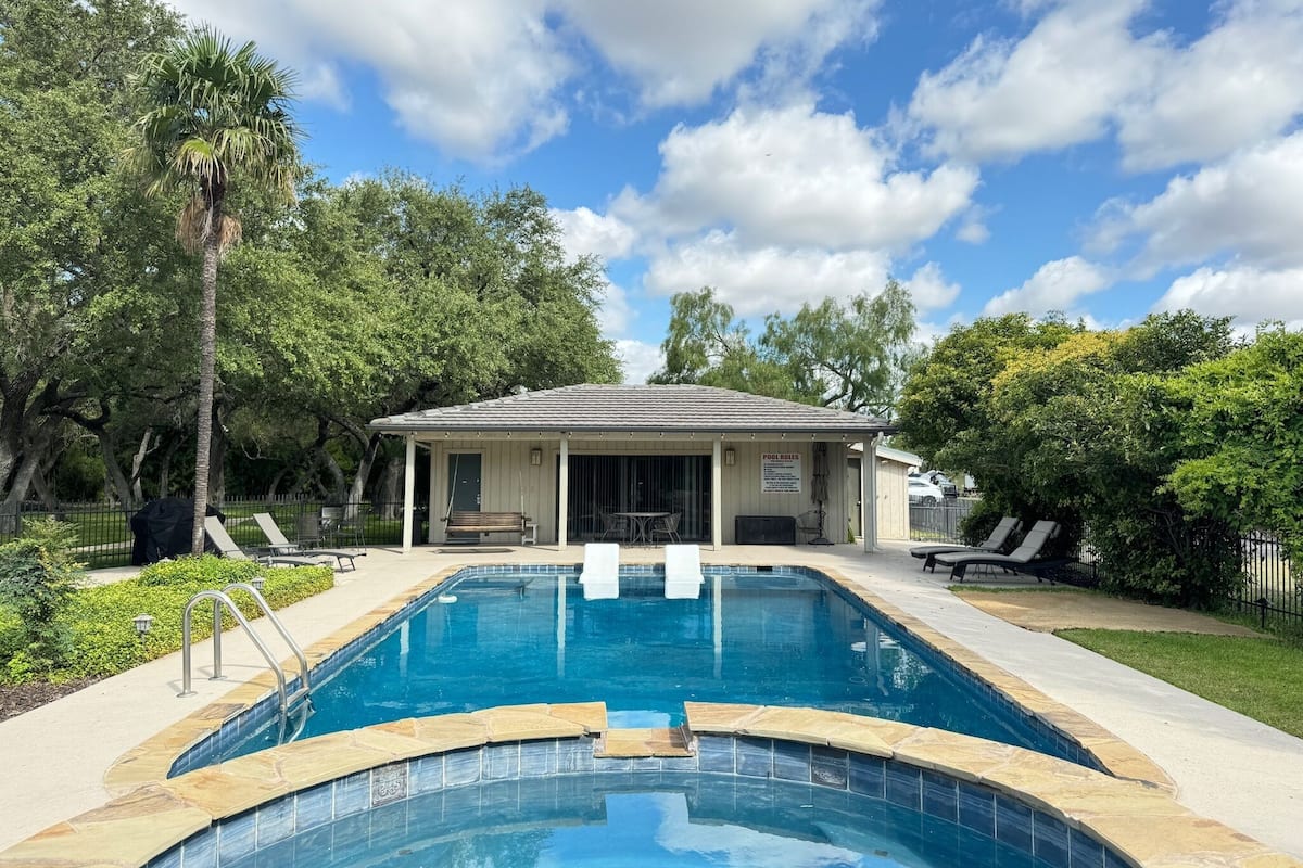 A pool area with a covered pavilion, lounge chairs, and a clear blue sky.