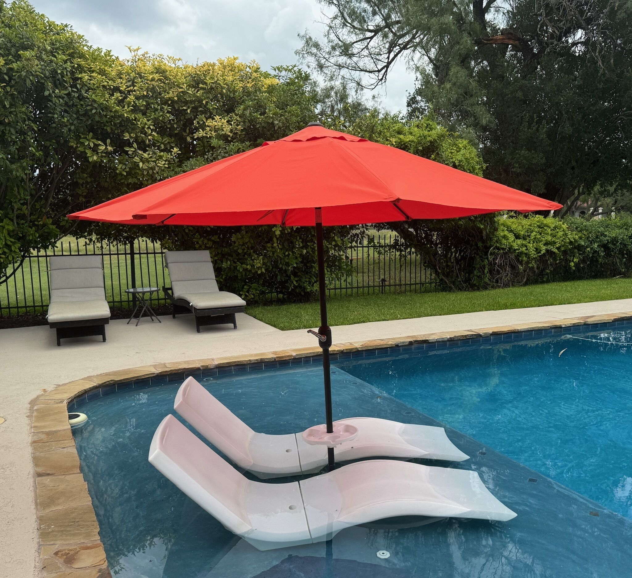 A pool area with a red umbrella, two lounge chairs, and a poolside setting.