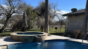 Una piscina azul cristalina con bordes de piedra, rodeada por una zona pavimentada y una valla.