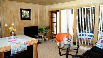 A living room with wooden paneling, a television, a glass table, a sofa, and a sliding glass door leading to a balcony.
