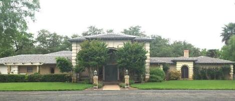A two-story house with a central entrance, surrounded by a well-maintained lawn and trees.