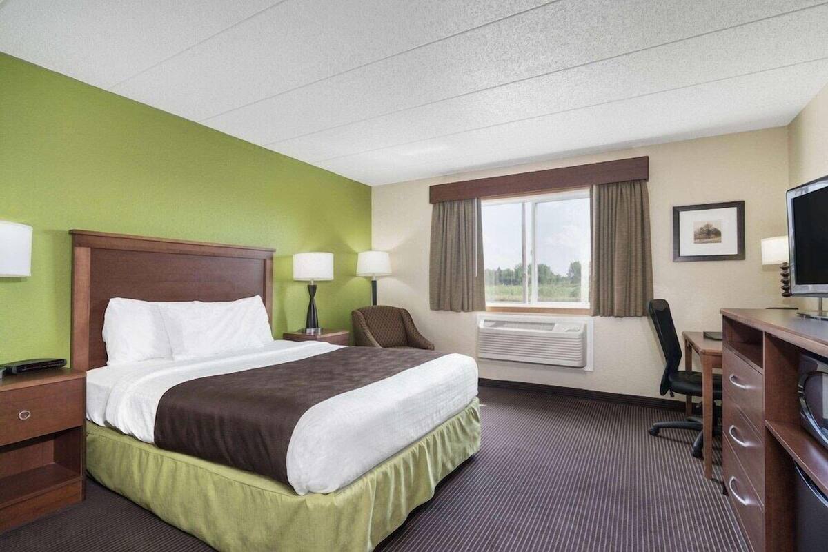 A hotel room with a bed, desk, chair, television, and window with curtains.