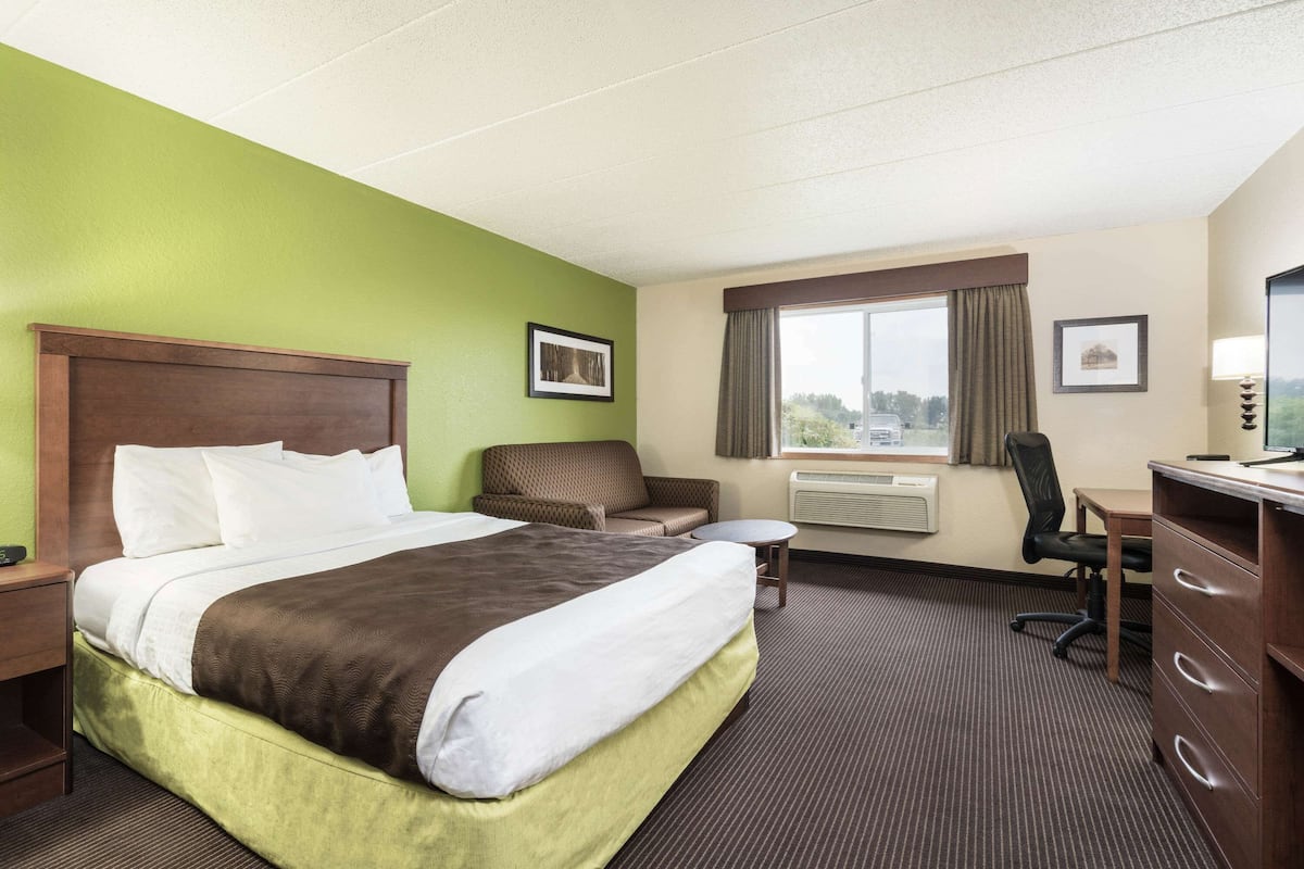 A hotel room with a large bed, a desk, a chair, a small table, and a TV.