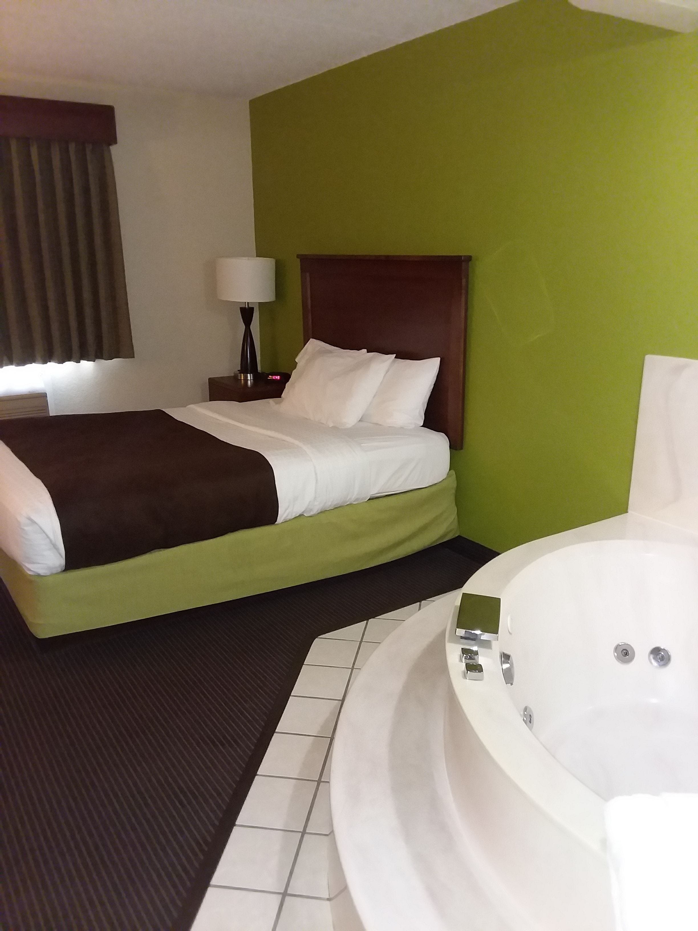 Una habitación de hotel con una cama, una mesita de noche con lámpara y una bañera.