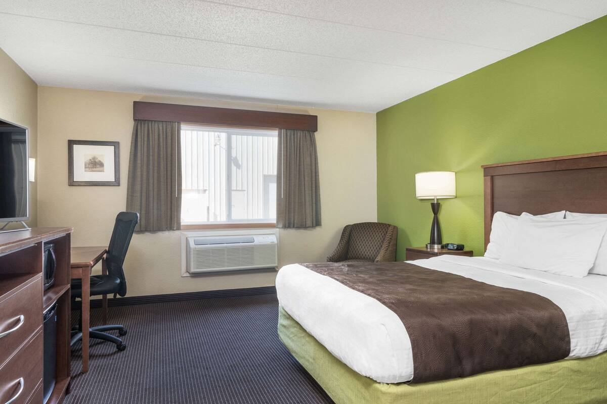 A hotel room with a bed, desk, chair, and a window with curtains.