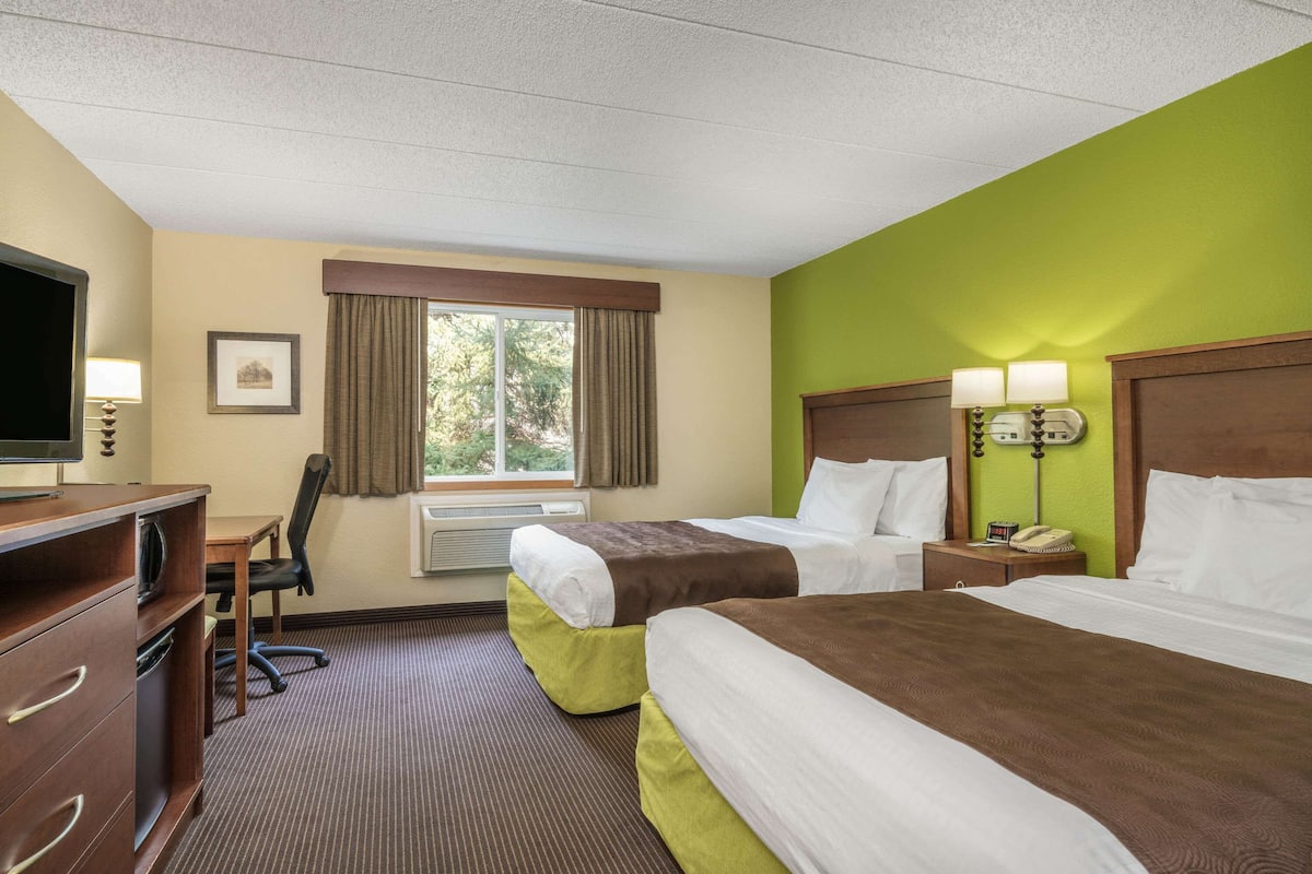 A hotel room with two beds, a desk with a chair, a television, and a window with curtains.
