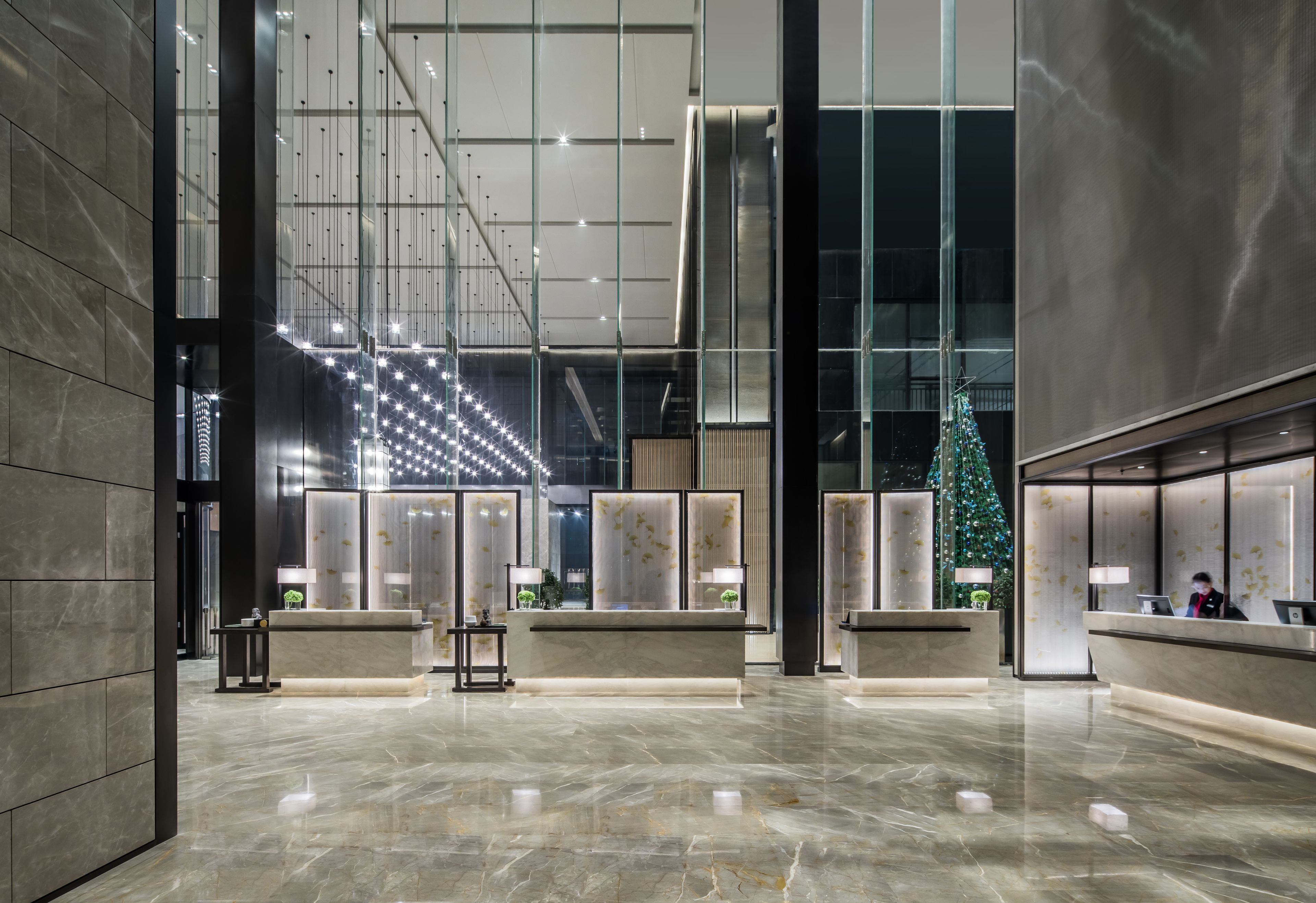A spacious lobby with a marble floor, modern reception desks, and a large Christmas tree.