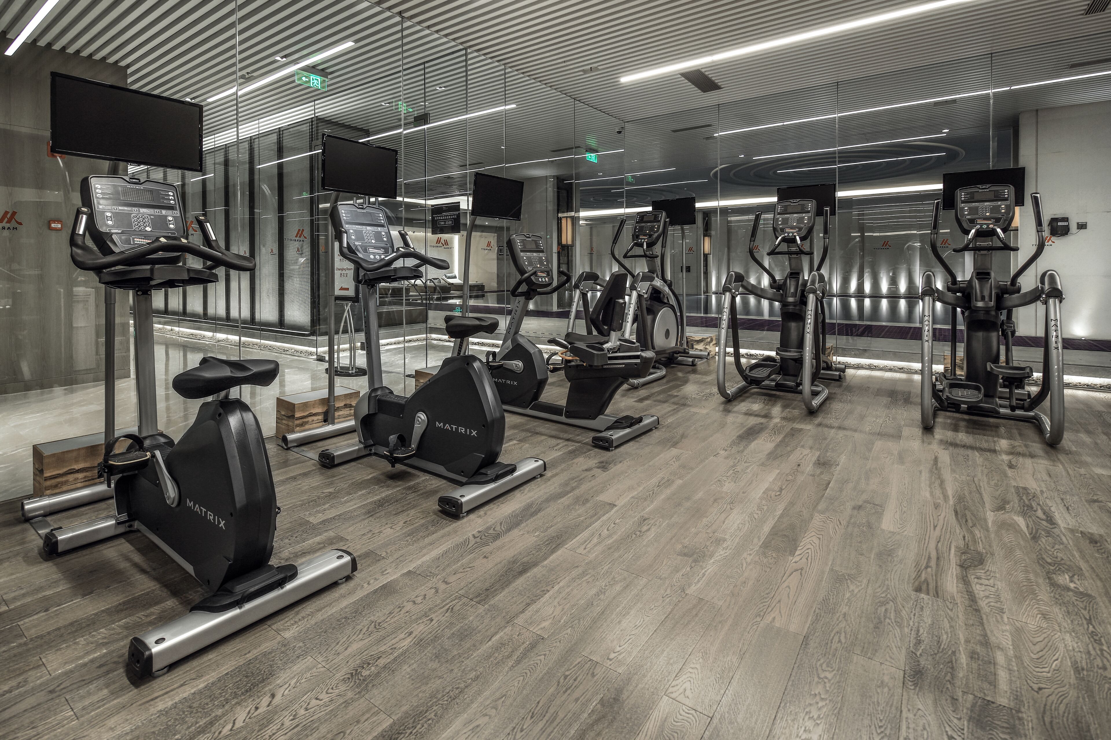 Et moderne fitnesscenter med flere motionscykler og løbebånd, med trægulv og glasvægge.