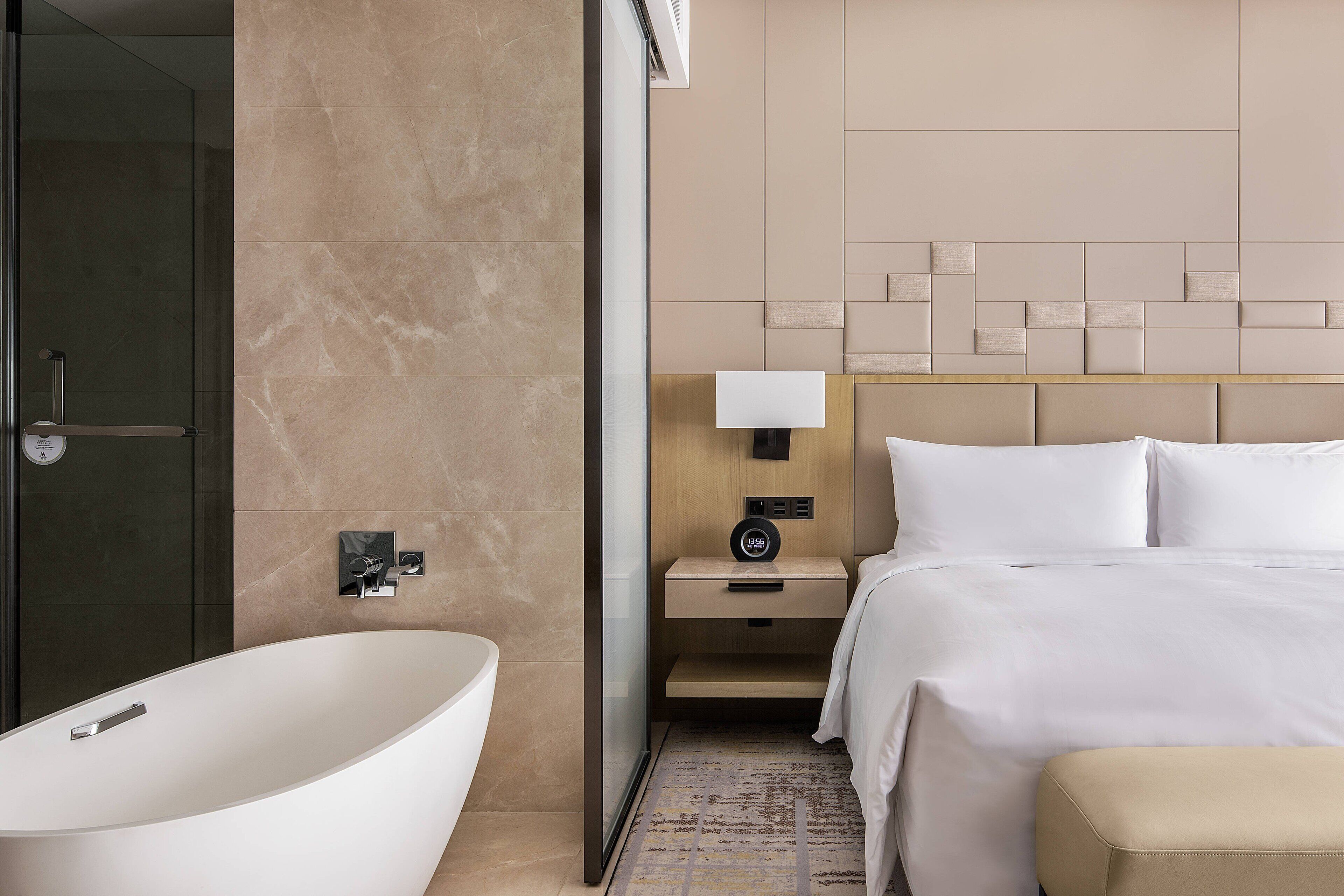 Une chambre d’hôtel moderne avec une grande baignoire, un lit soigneusement fait et une table de chevet avec une lampe.