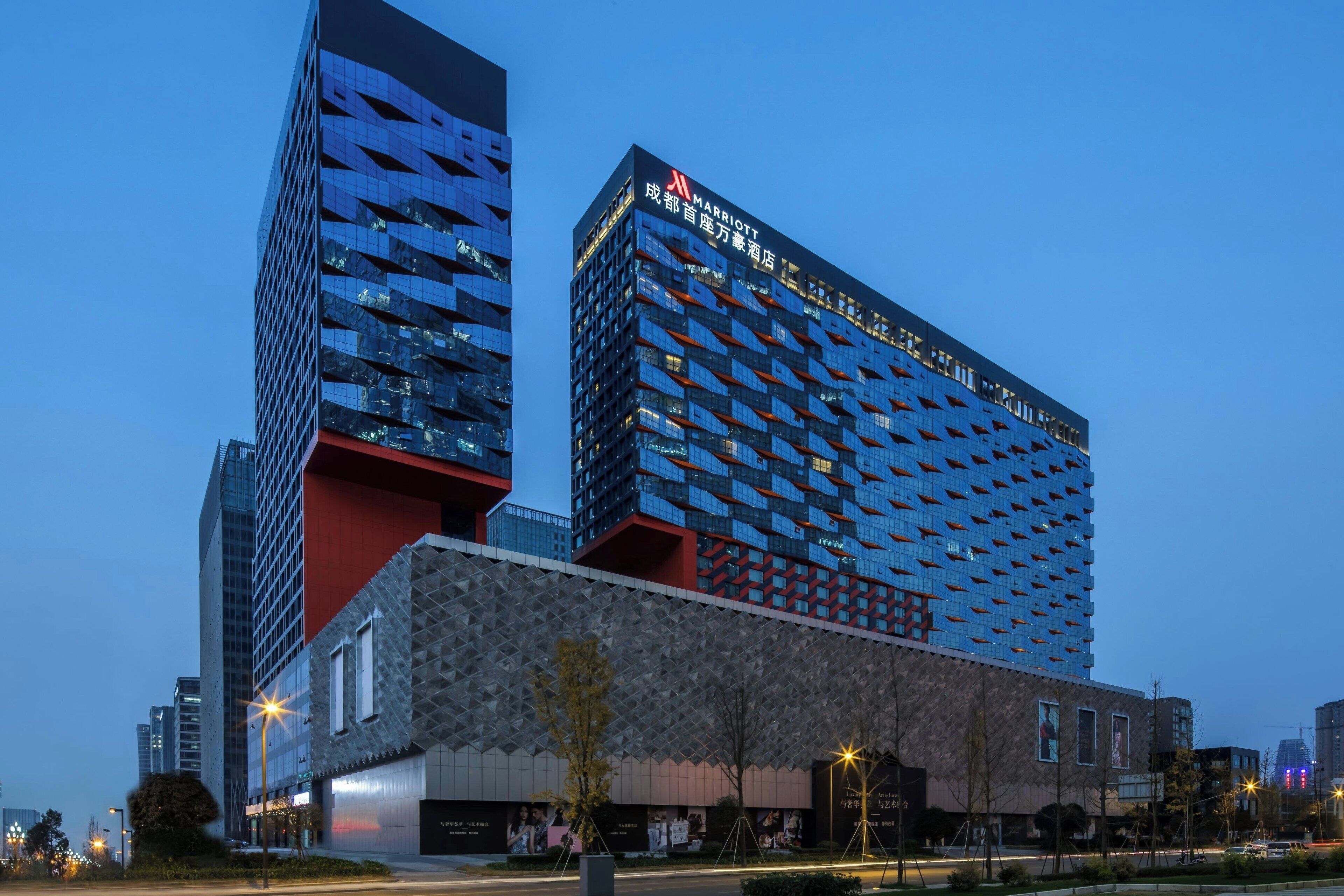 A modern hotel with a distinctive facade featuring a mix of reflective and matte surfaces, large windows, and a prominent signage.