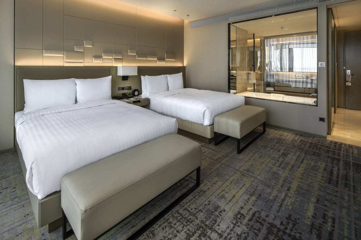 Ein Hotelzimmer mit zwei Betten, einer Bank, einem großen Spiegel und einem gemusterten Teppich.