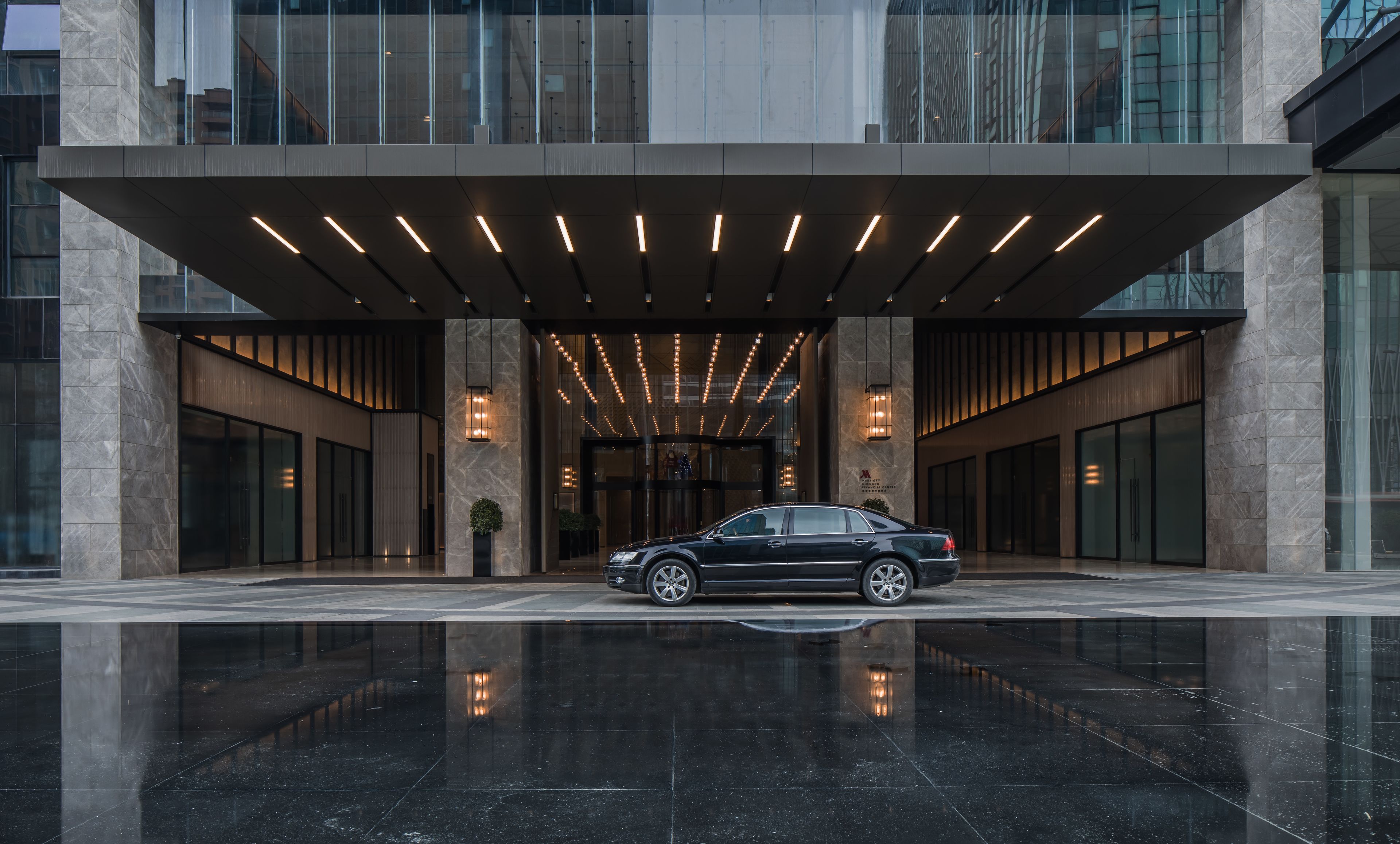 A modern building entrance with a black car parked in front, large glass windows, and a reflective black floor.