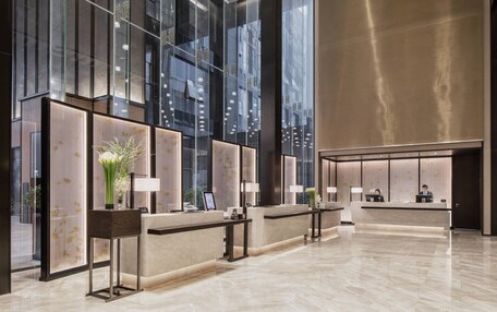 A modern hotel reception area with glass partitions, marble counters, and a spacious lobby.
