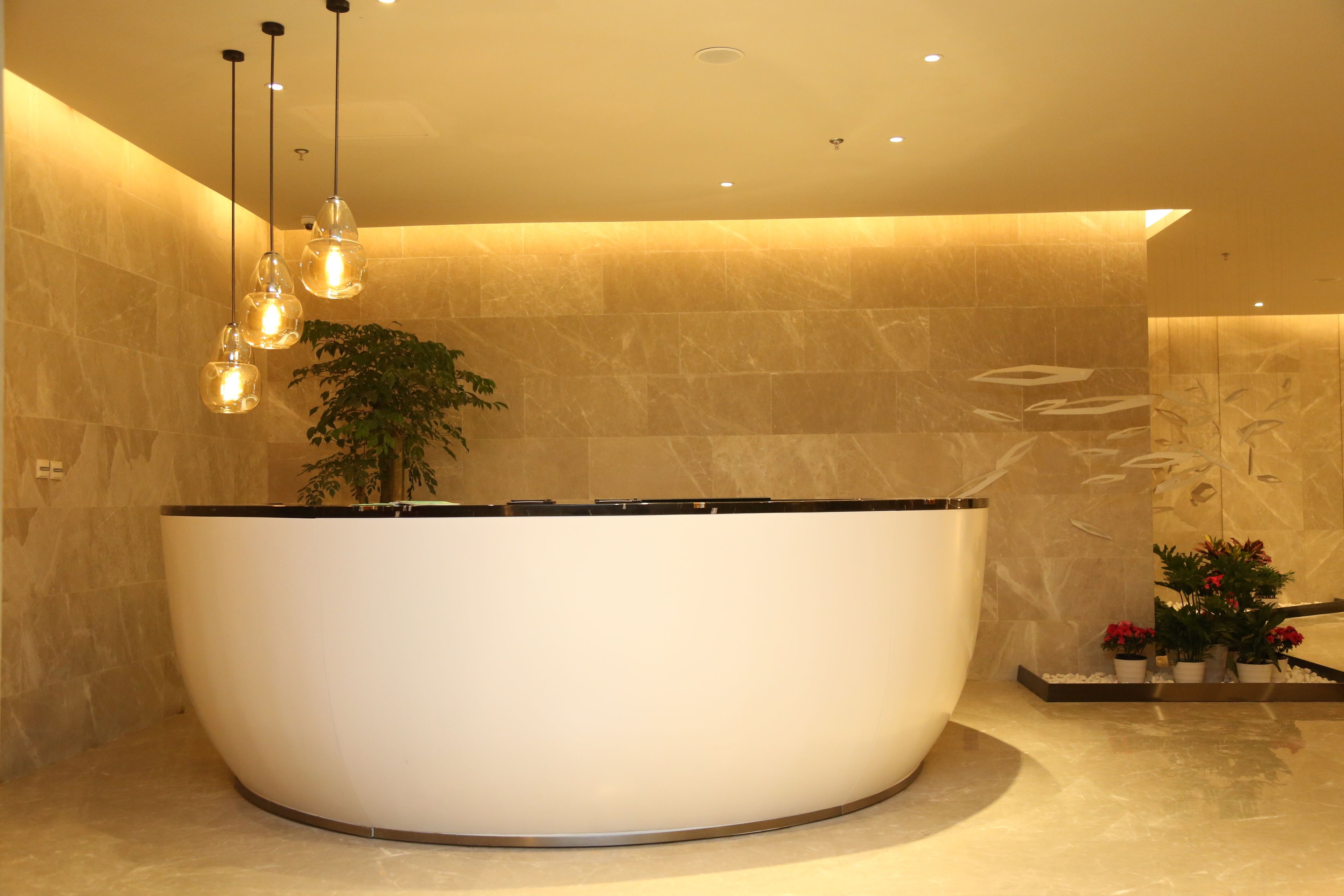 A modern bathroom with a large, curved bathtub, a potted plant, and pendant lighting.