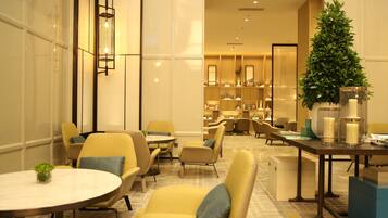 A hotel lobby with yellow seating, a reception desk, and a large potted plant.