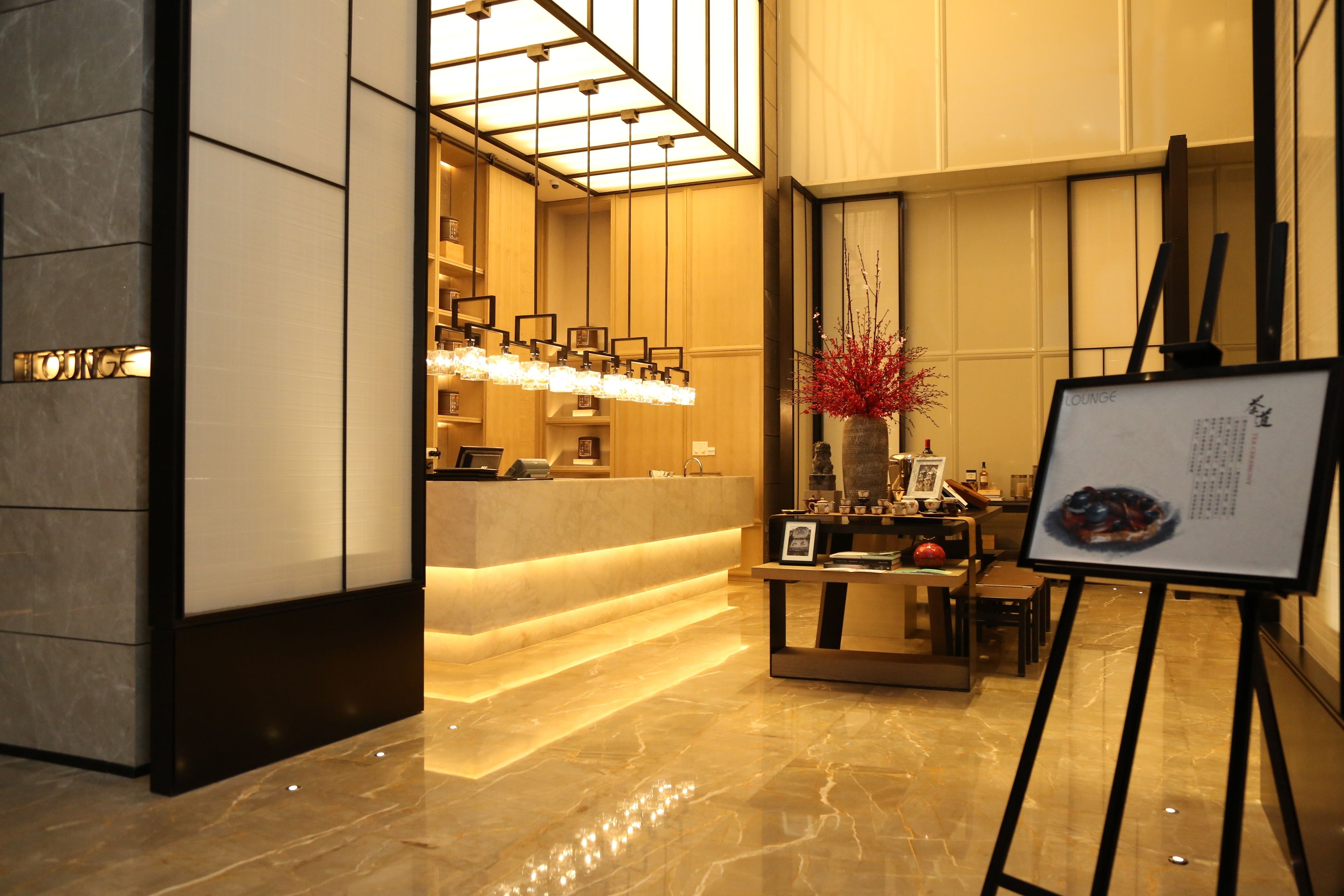 A lobby with a reception desk, a seating area with a vase of red flowers, and a framed menu on a stand.