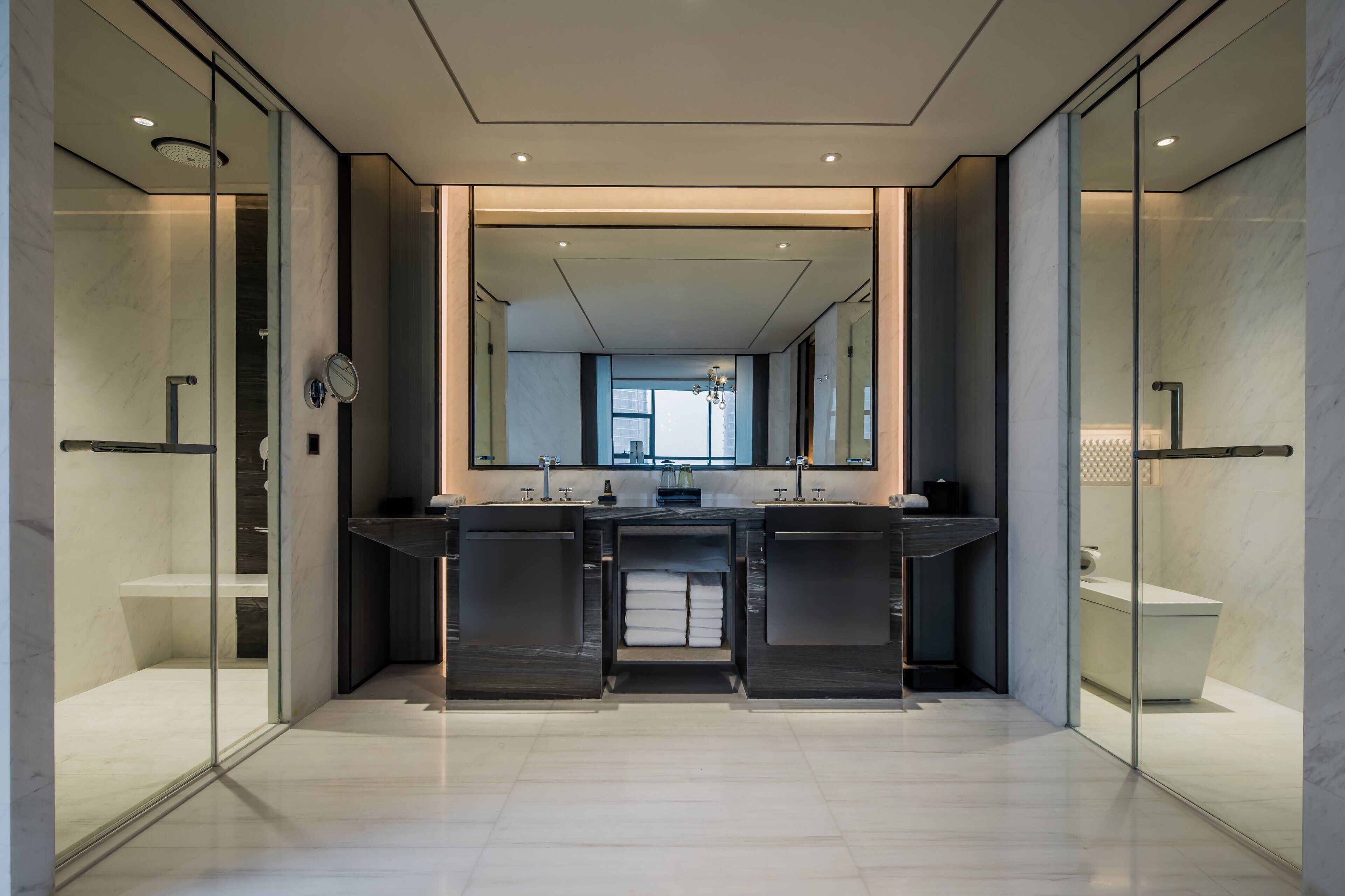 A modern bathroom with a large mirror, two sinks, and a glass shower enclosure.