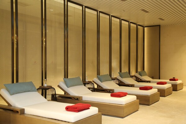 A row of sunbeds with towels, a small table, and a wall with vertical panels.