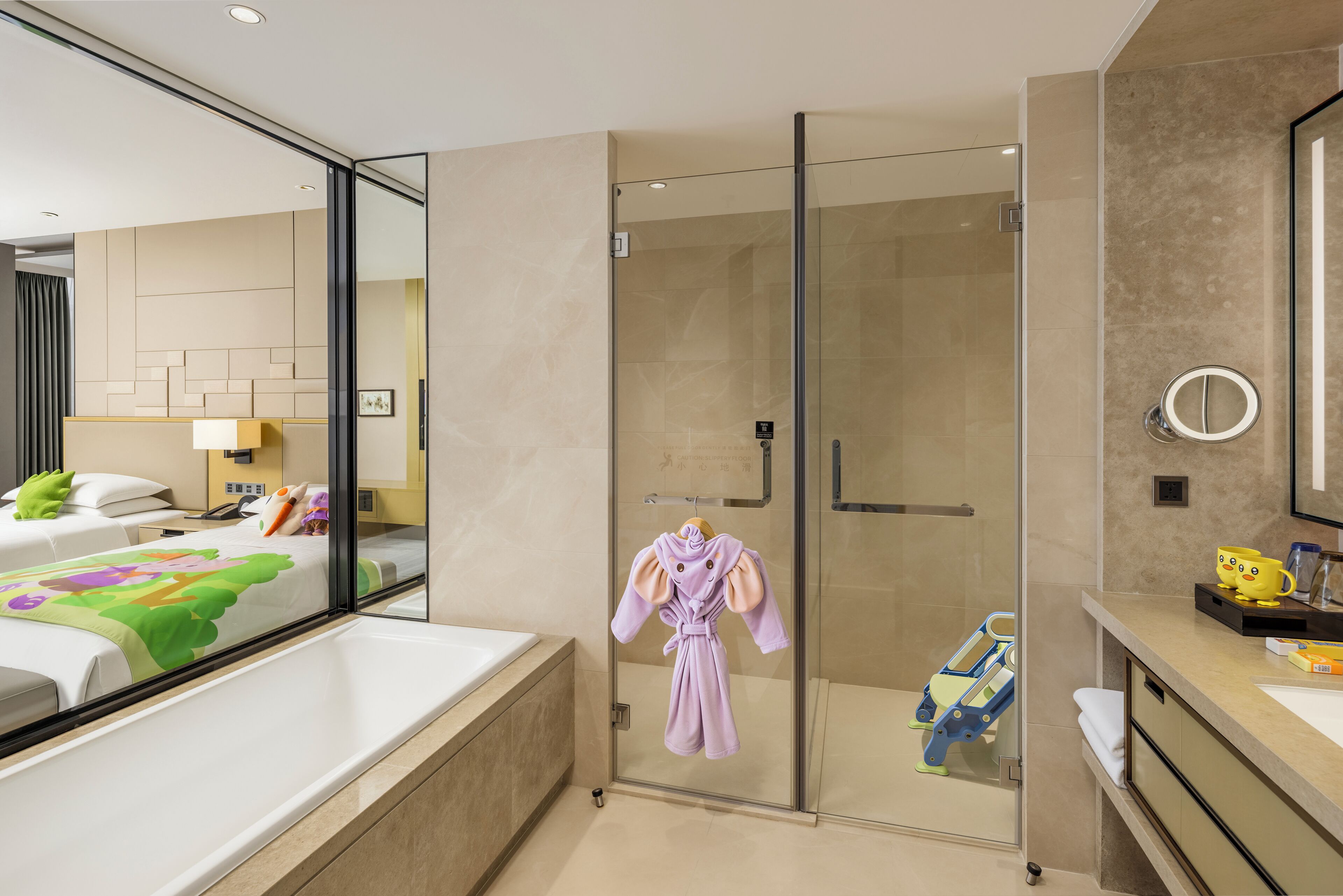 A hotel room with a glass-enclosed shower, a bed with a colorful bedspread, and a bathroom with a sink and mirror.