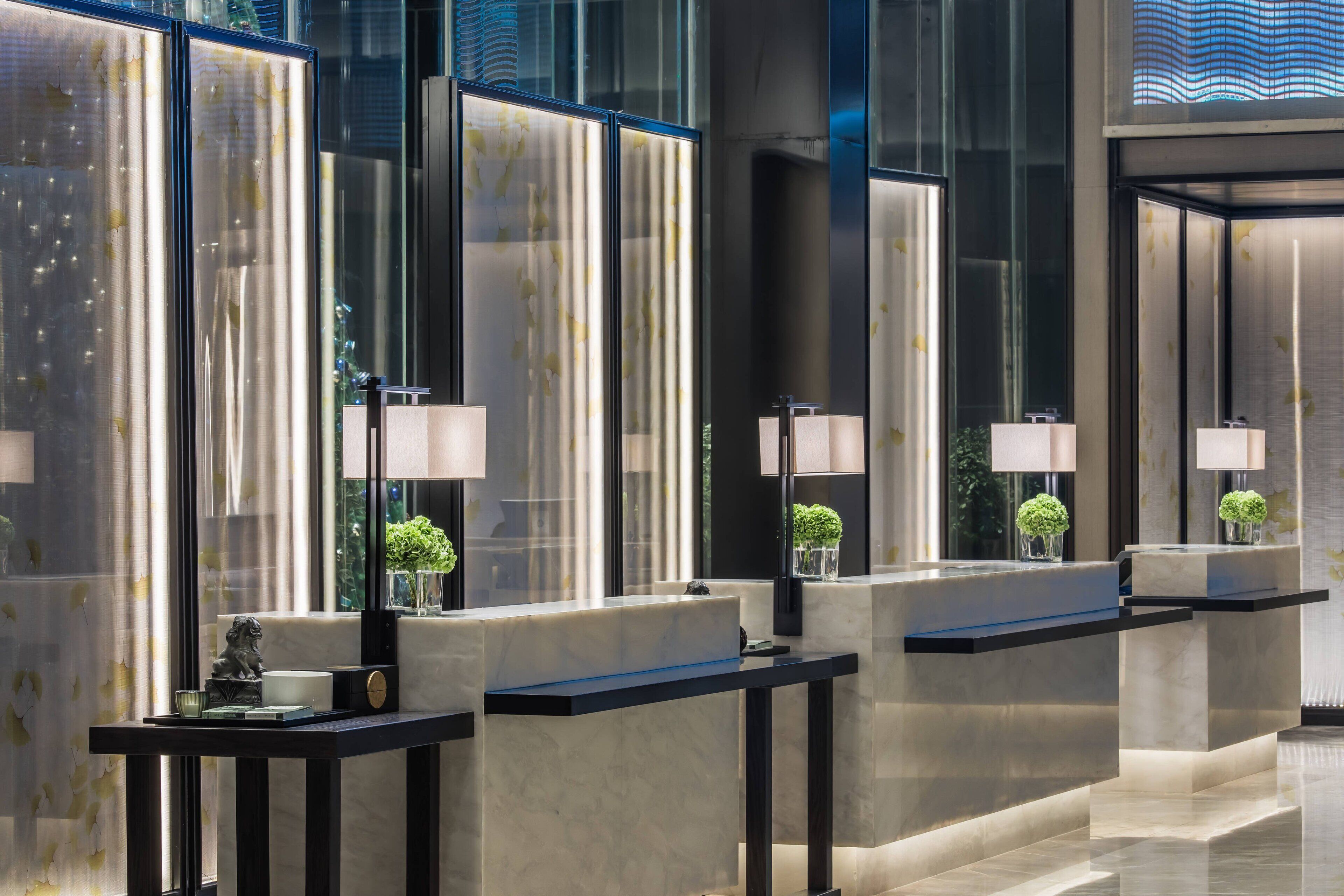 A modern hotel lobby with marble counters, black-framed mirrors, and small potted plants.