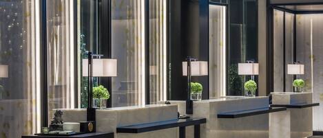 Een moderne hotellobby met marmeren balies, spiegels met zwarte omlijsting en kleine potplanten.