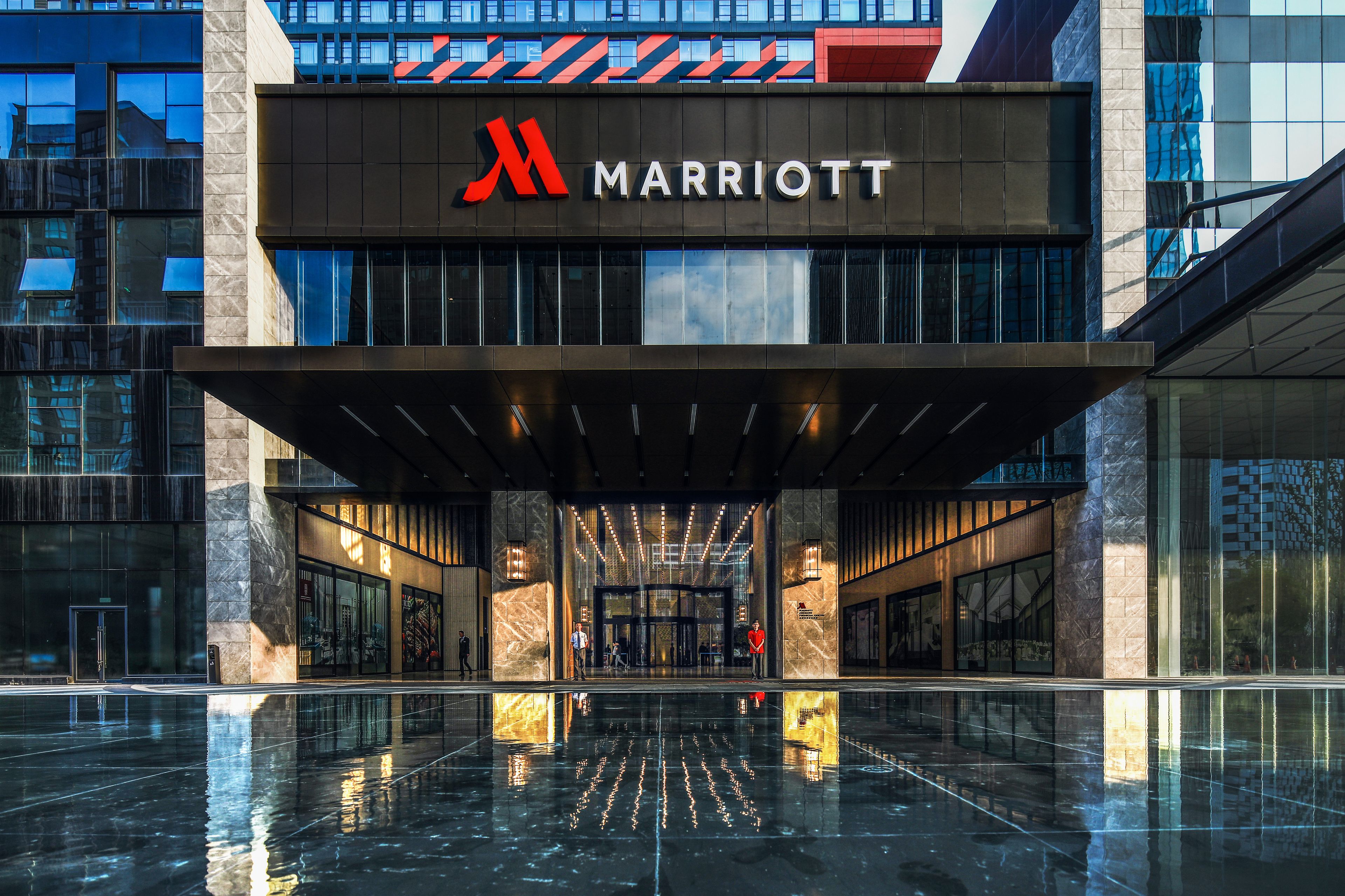 A modern Marriott hotel entrance with a reflective black floor, large glass windows, and a prominent red logo.