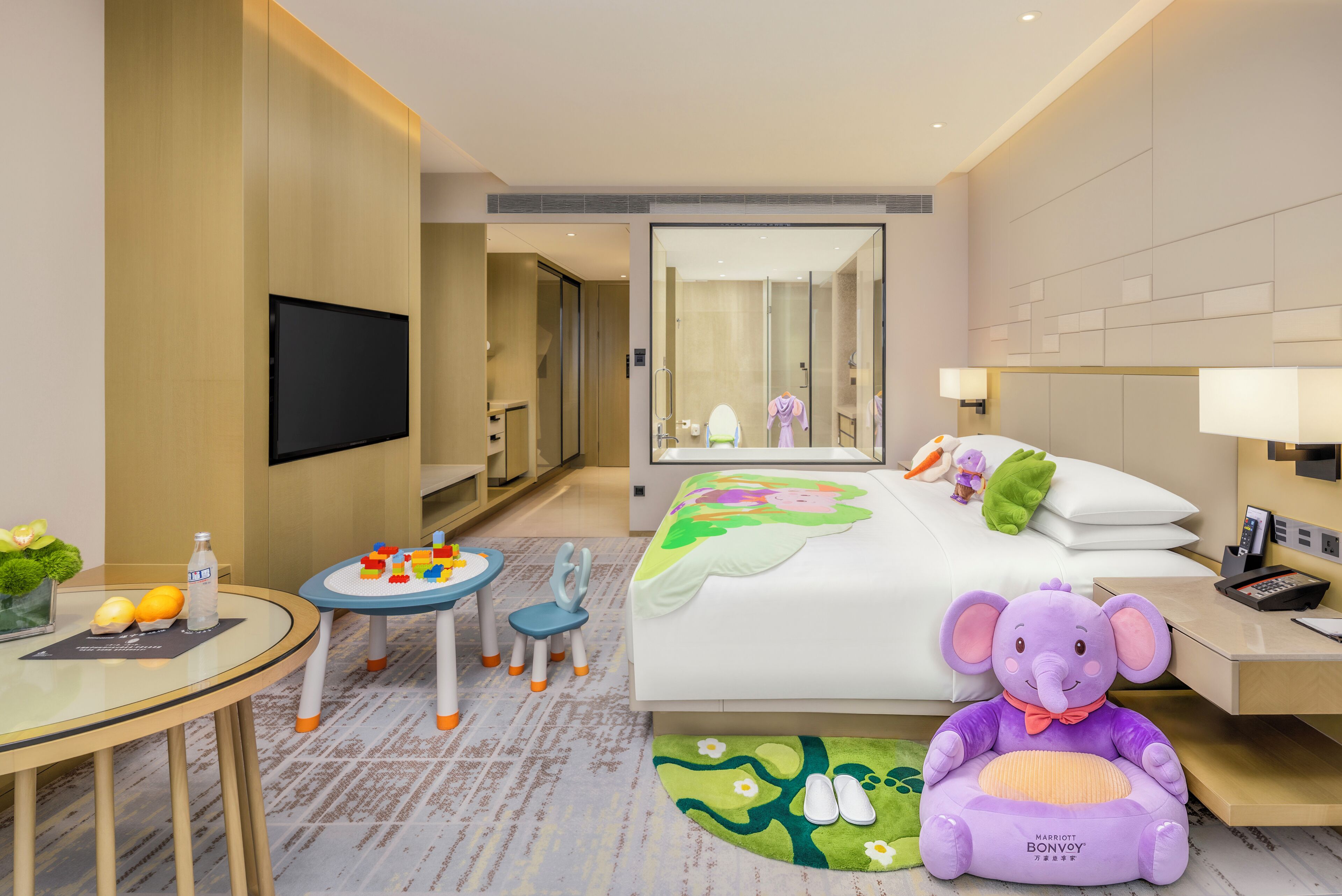 A hotel room with a bed, a desk, a chair, a television, a mirror, and a plush toy.
