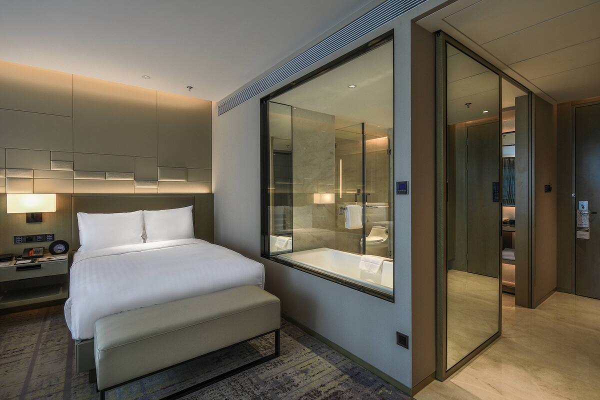 Ein modernes Hotelzimmer mit einem großen Bett, einem verglasten Badezimmer und einem begehbaren Kleiderschrank.