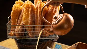 A hand pouring syrup over churros in a basket.