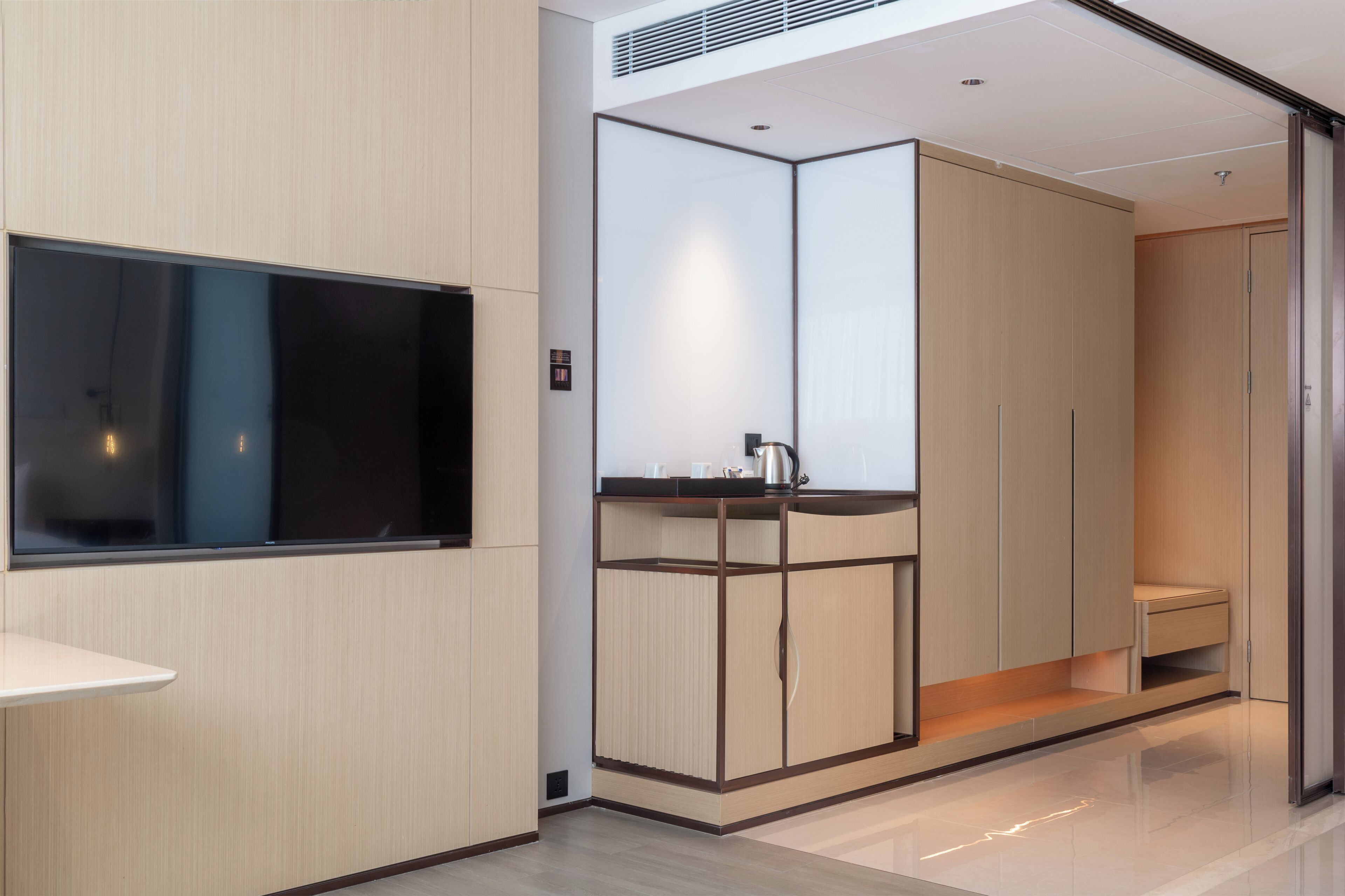 Una habitación de hotel moderna con un televisor de pantalla plana grande, un escritorio integrado con hervidor de agua y un armario con puertas de espejo.