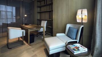 Une chambre d’hôtel moderne équipée d’un bureau, de deux chaises, d’un canapé, d’une bibliothèque et d’une lampe.