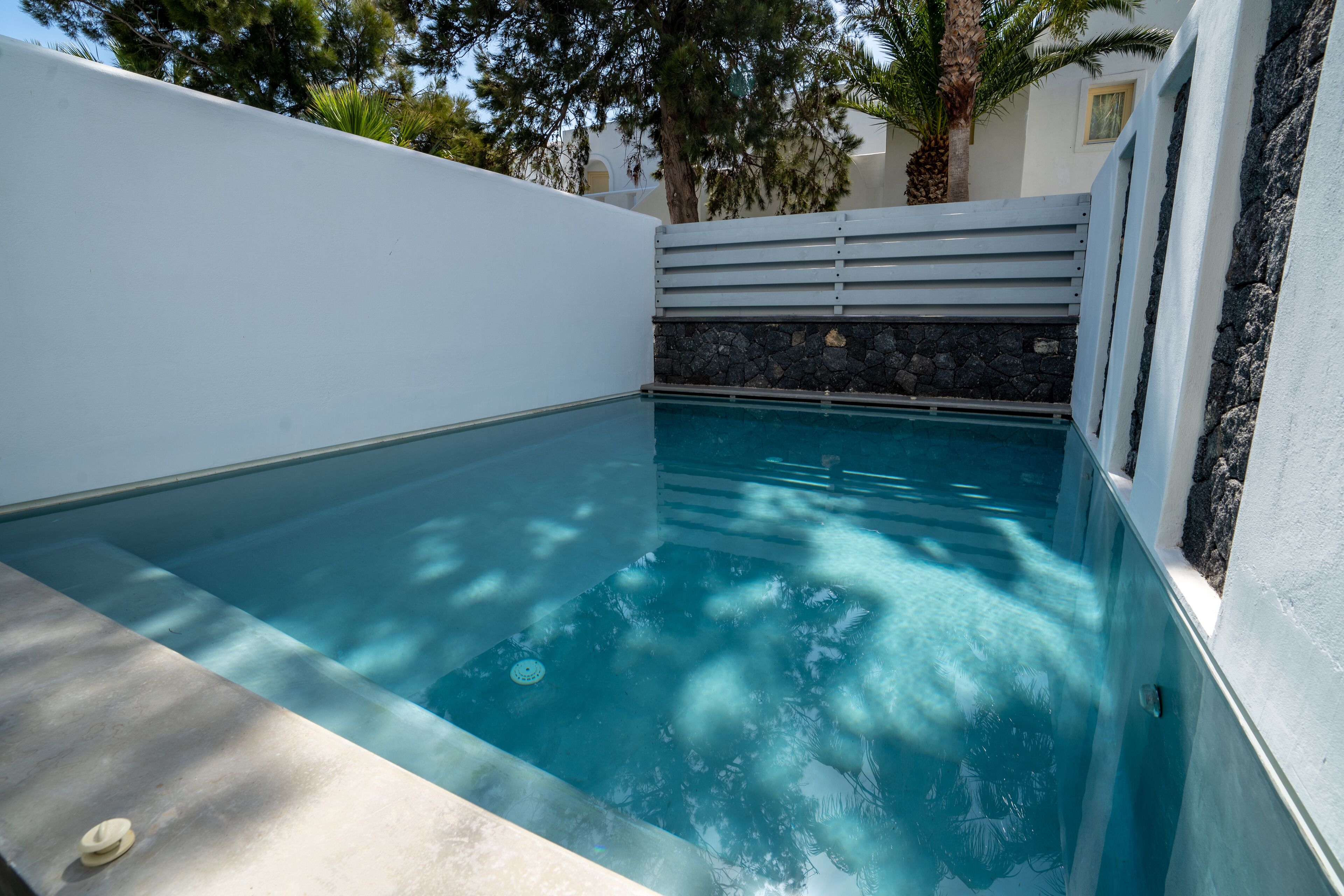 A swimming pool with clear blue water, surrounded by white walls and a stone wall.