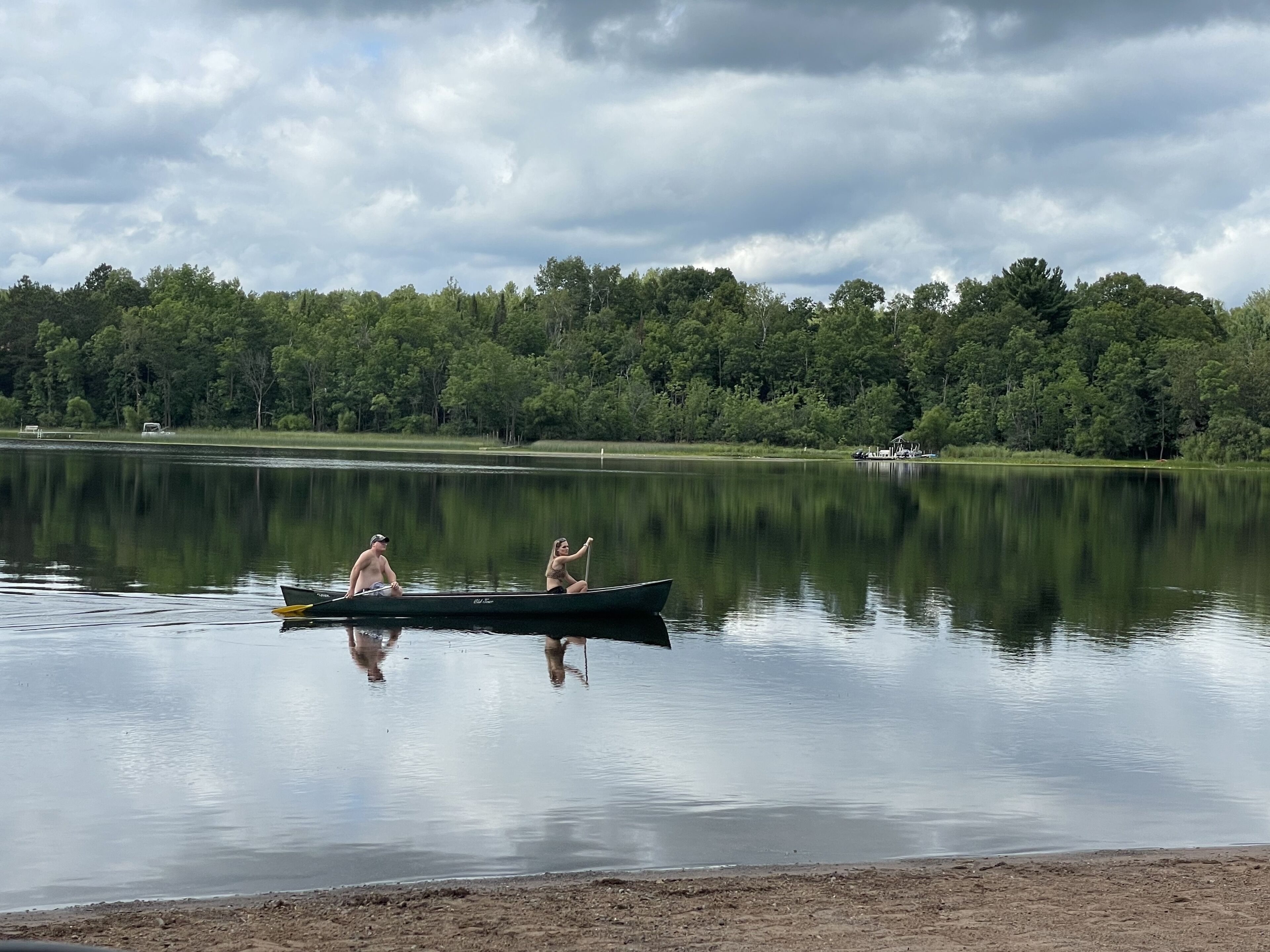 Un lago tranquilo con dos canoas, una orilla boscosa y un cielo nublado.