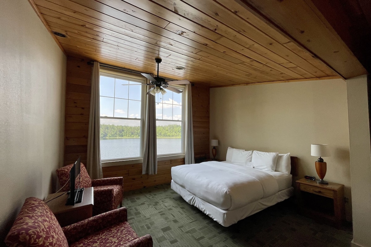A bedroom with a bed, two bedside tables, a chair, a window with curtains, and a ceiling fan.