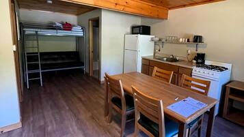A compact kitchen with a wooden table and chairs, a refrigerator, a microwave, and a stove.