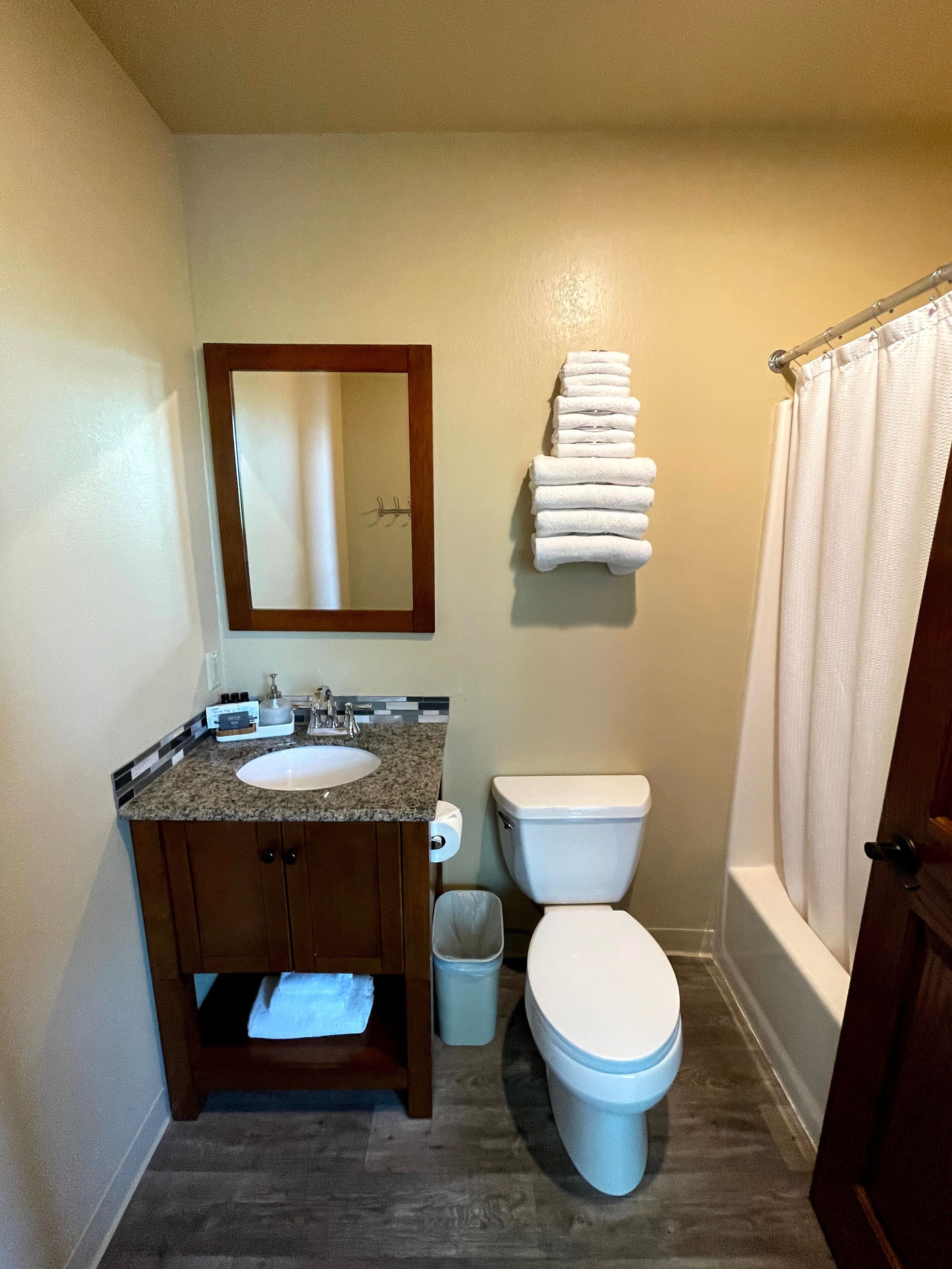 A bathroom with a sink, mirror, toilet, and a stack of towels.