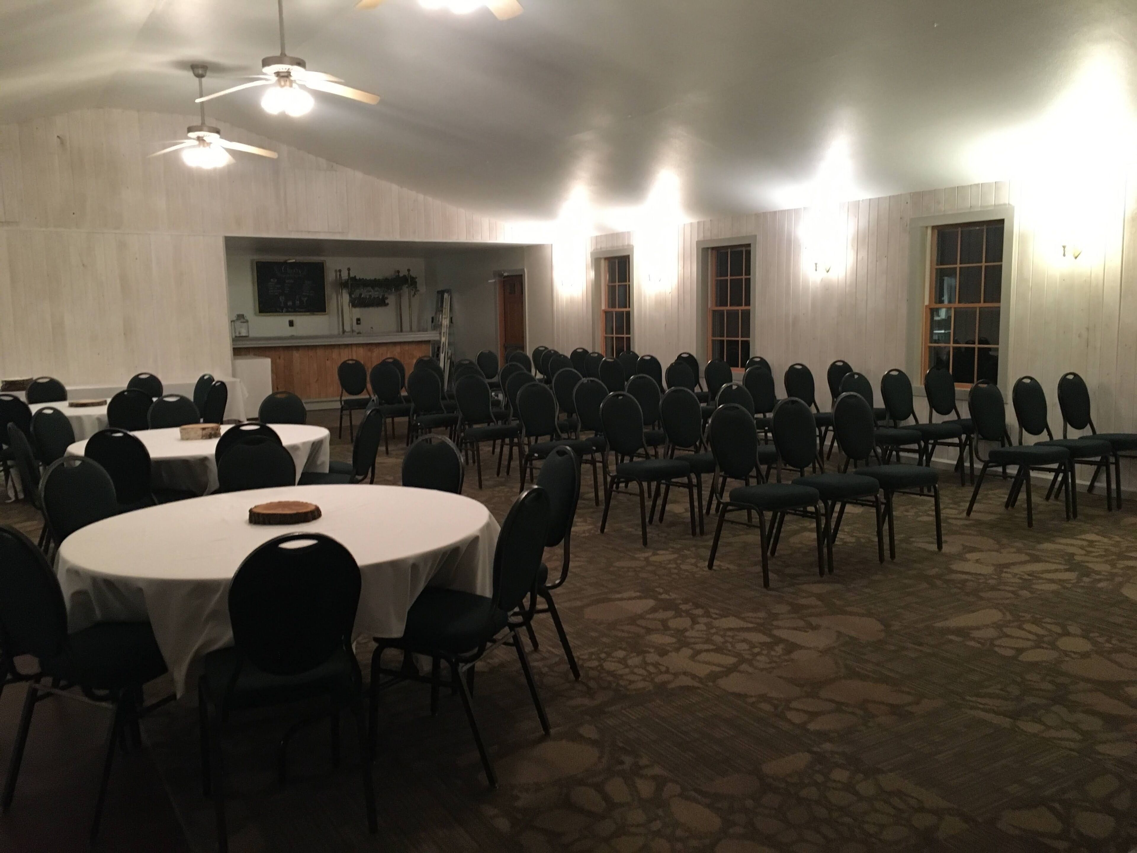 A conference room with round tables and chairs, a stage, and a kitchenette area.