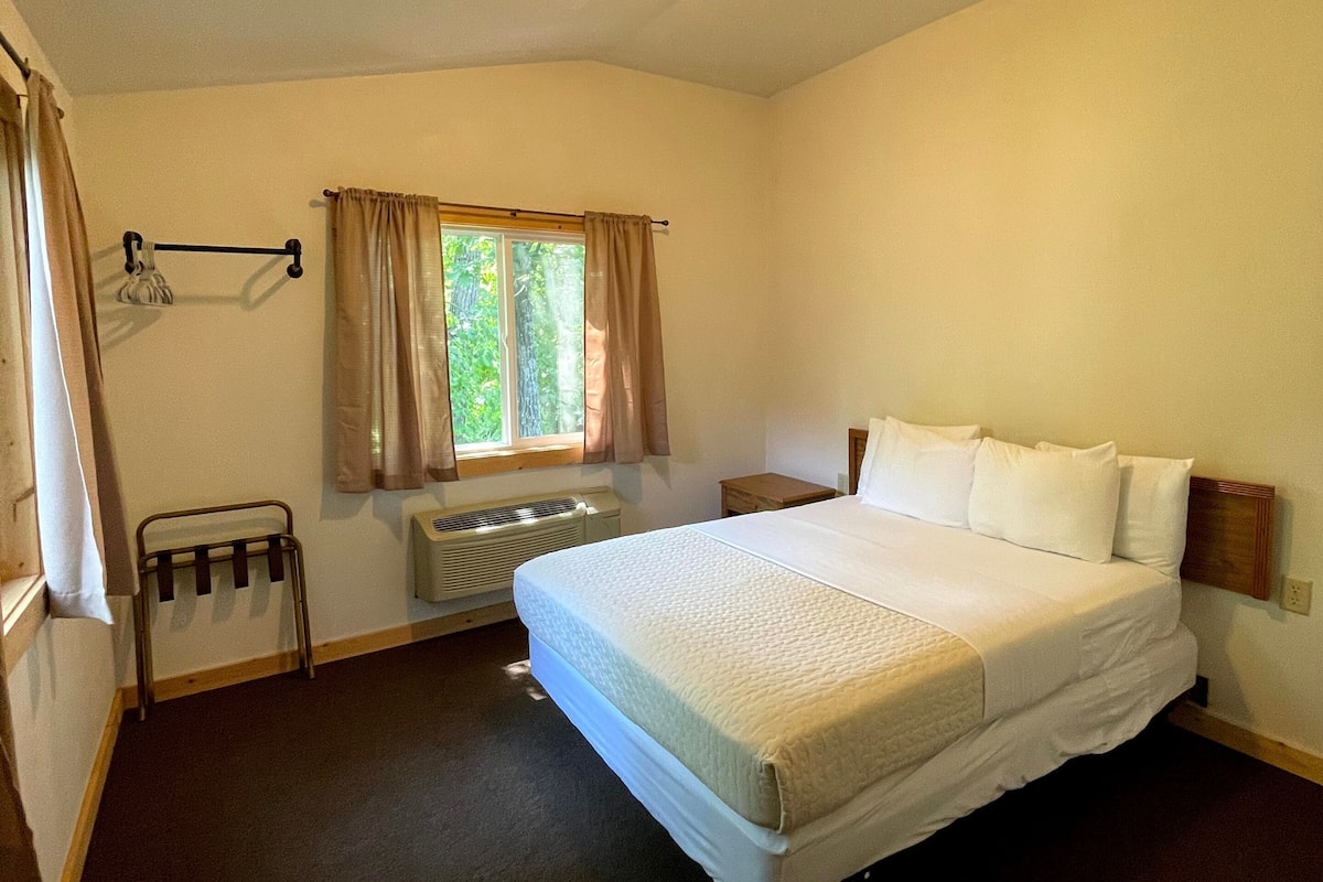 A hotel room with a large bed, a window with curtains, a radiator, and a small table.