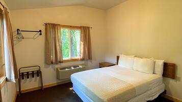 Une chambre d’hôtel avec un grand lit, une fenêtre avec des rideaux, un radiateur et une petite table.