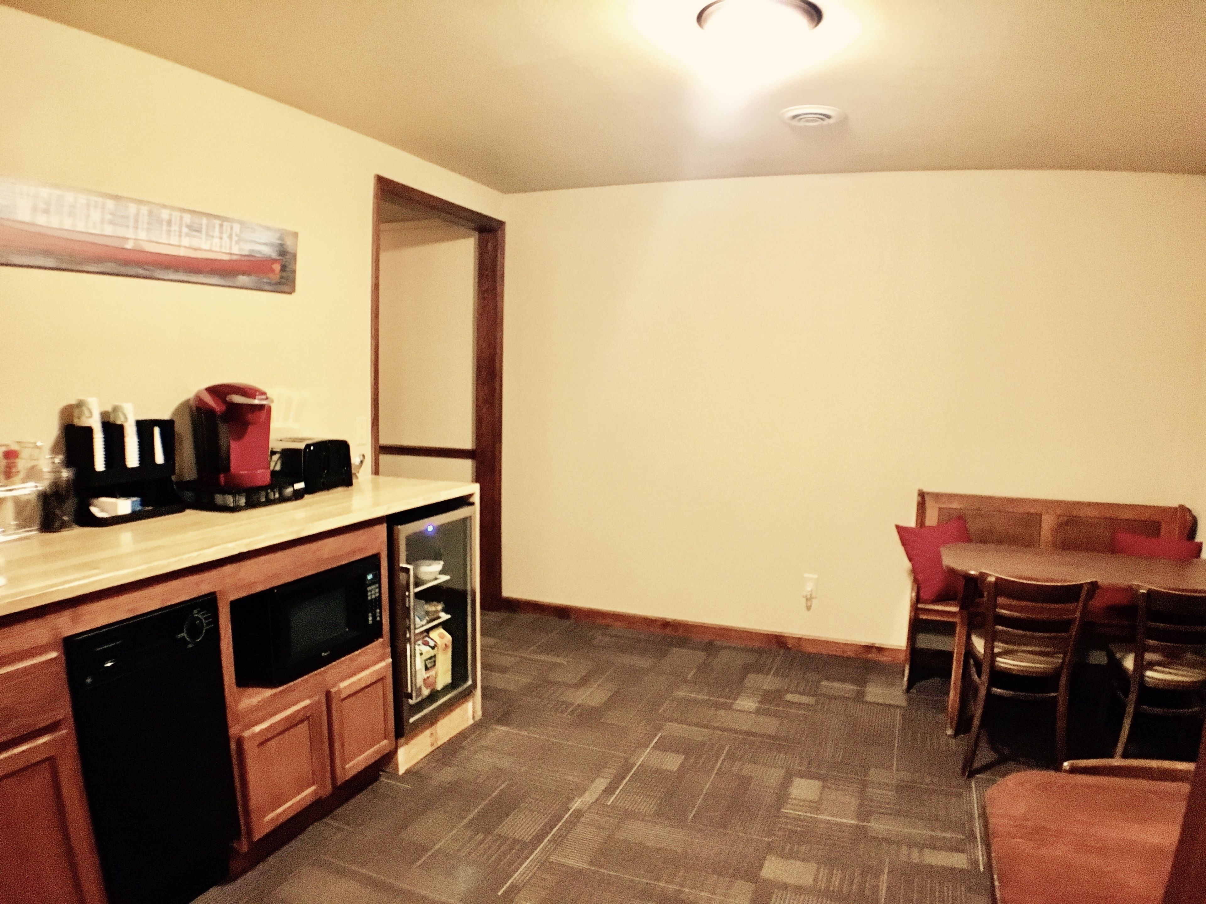 A compact kitchen with a dishwasher, microwave, and coffee maker on the counter. A dining table with chairs is in the background.