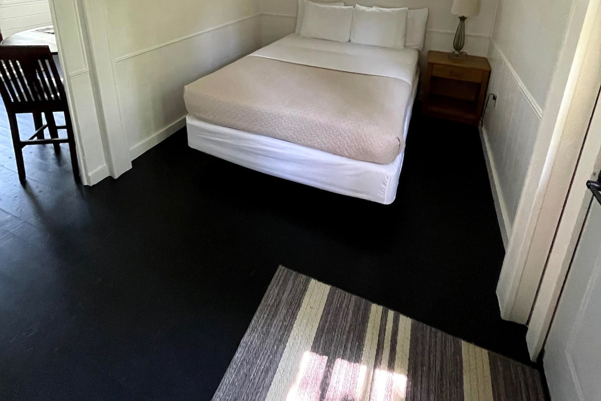 A bedroom with a bed, a nightstand, a window, and a chair.