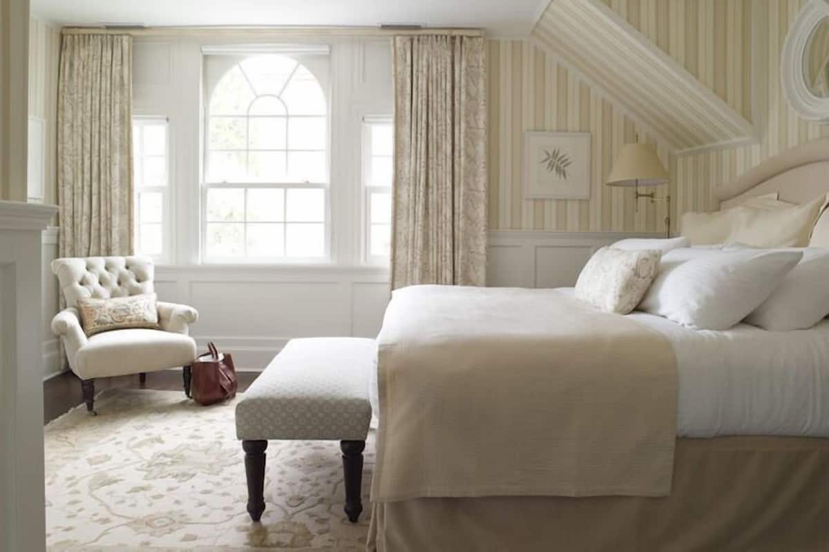 A bedroom with a large bed, a chair, and a window with curtains.