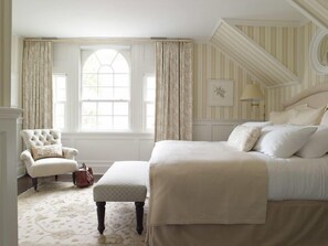 Une chambre à coucher avec un grand lit, une chaise et une fenêtre avec des rideaux.