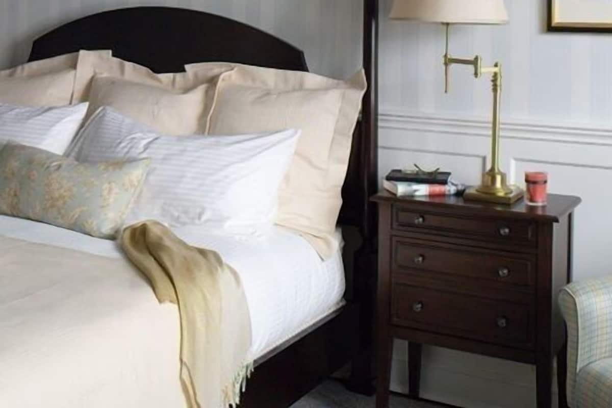 A neatly made bed with multiple pillows and a bedside table with a lamp and a book.