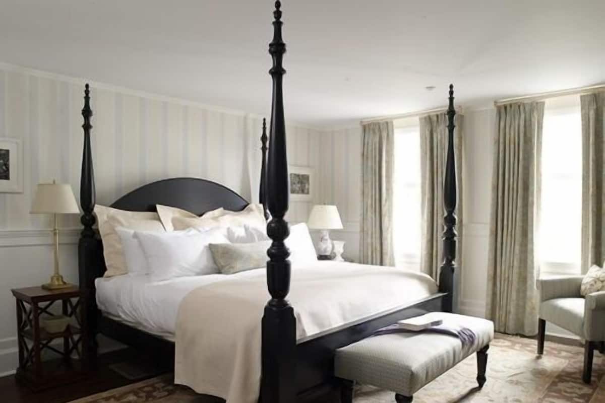 A four-poster bed with white linens, a matching bench, and two bedside tables with lamps.