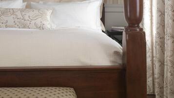 Una cama bien hecha con tablero de madera, un reposapiés a juego y una mesita de noche con lámpara.