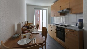 Cocina compacta con armarios de madera, una estufa y un comedor con sillas y una mesa para dos personas.